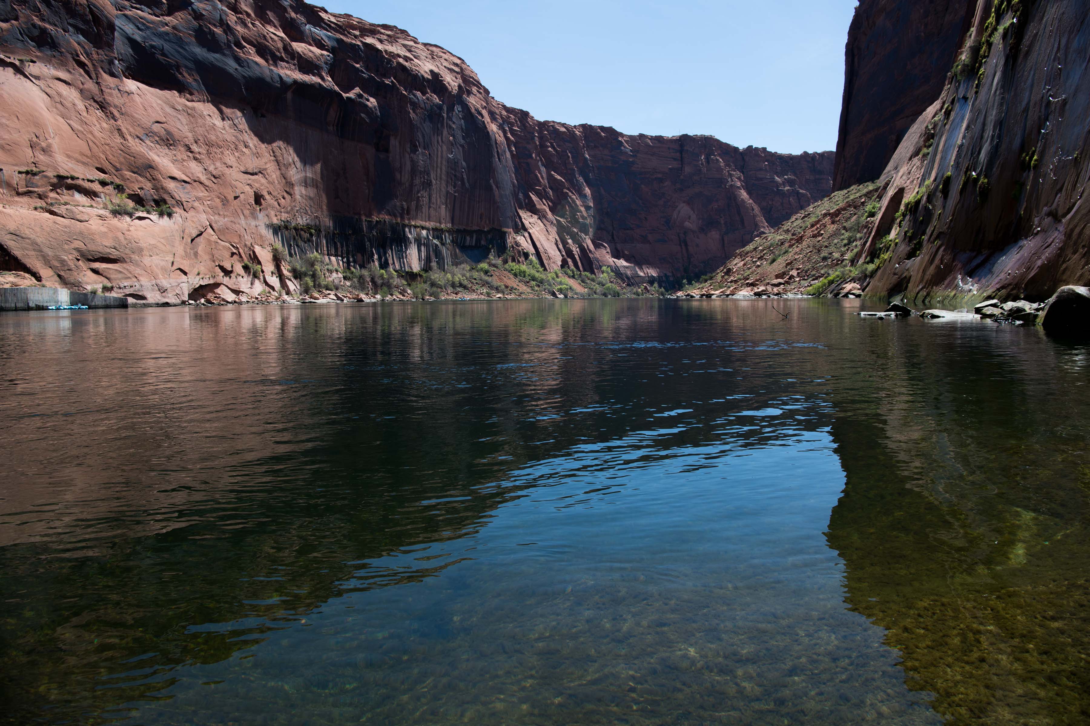 The Colorado River flowing between sandstone cliffs. The sun is shining on the far cliffs.