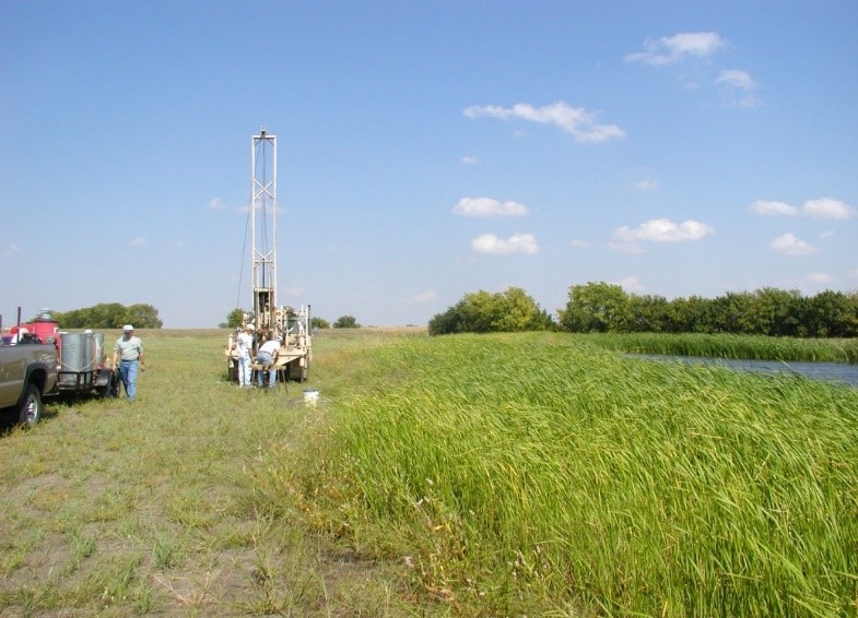 Photo of people constructing a small tower in a field with water in a ditch