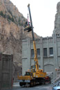 CAT Excavator being lifted onto to the roof of Shoshone Power Plant. The roof consists of 5 to 6 feet of earth and rocks over a concrete slab over steel trusses. The excavator was used to dig several test pits to determine the actual depth of the material as well as to determine the type of material used to coat the concrete slab. Photo by Mark Skoric.