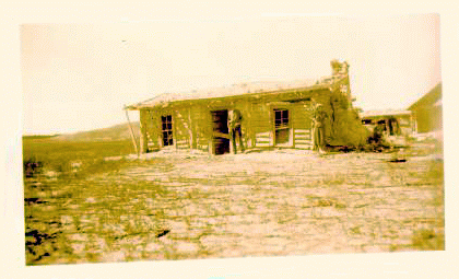 Two men standing infront of an old ramshackle ranch house. Sepia tone photo