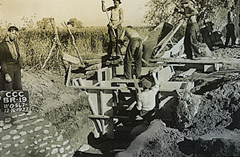 This 1937 photograph shows a CCC work crew building a form to replace an old wooden check structure with a concrete structure.  Note the new cobble and concrete wall to reduce erosion of the lateral. (Reclamation photograph)