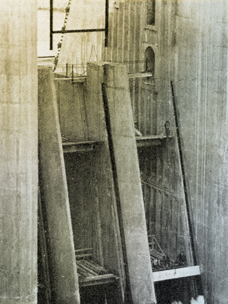Bird's eye view of workmen lowering one of the 240 concrete stop logs (each 13 ½ feet long and weighing 6 tons) into one of the slots in the spillway of the dam.