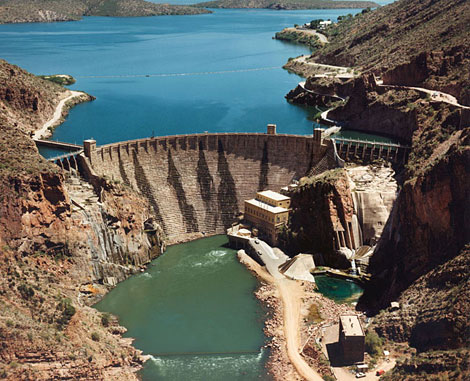 Theodore Roosevelt Dam, 1911. Water is being released through the outlet works to test the emergency gates. The dam structure is complete with operational powerhouse and transformer building. Reclamation photo.