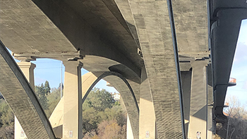 The underside of a road bridge reflected by still water in low light.