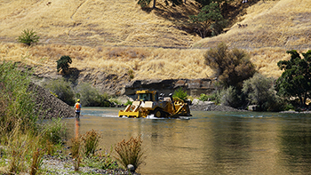 Construction equipment and crew are partially submerged while operating in a stream.