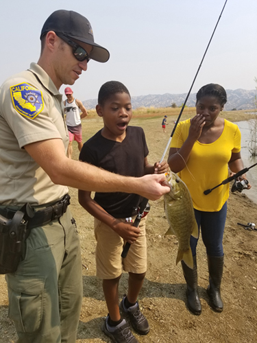 Game warden holds fish that child caught.