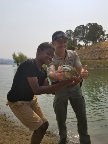 Child excited as game warden holds fish and poses for photo.