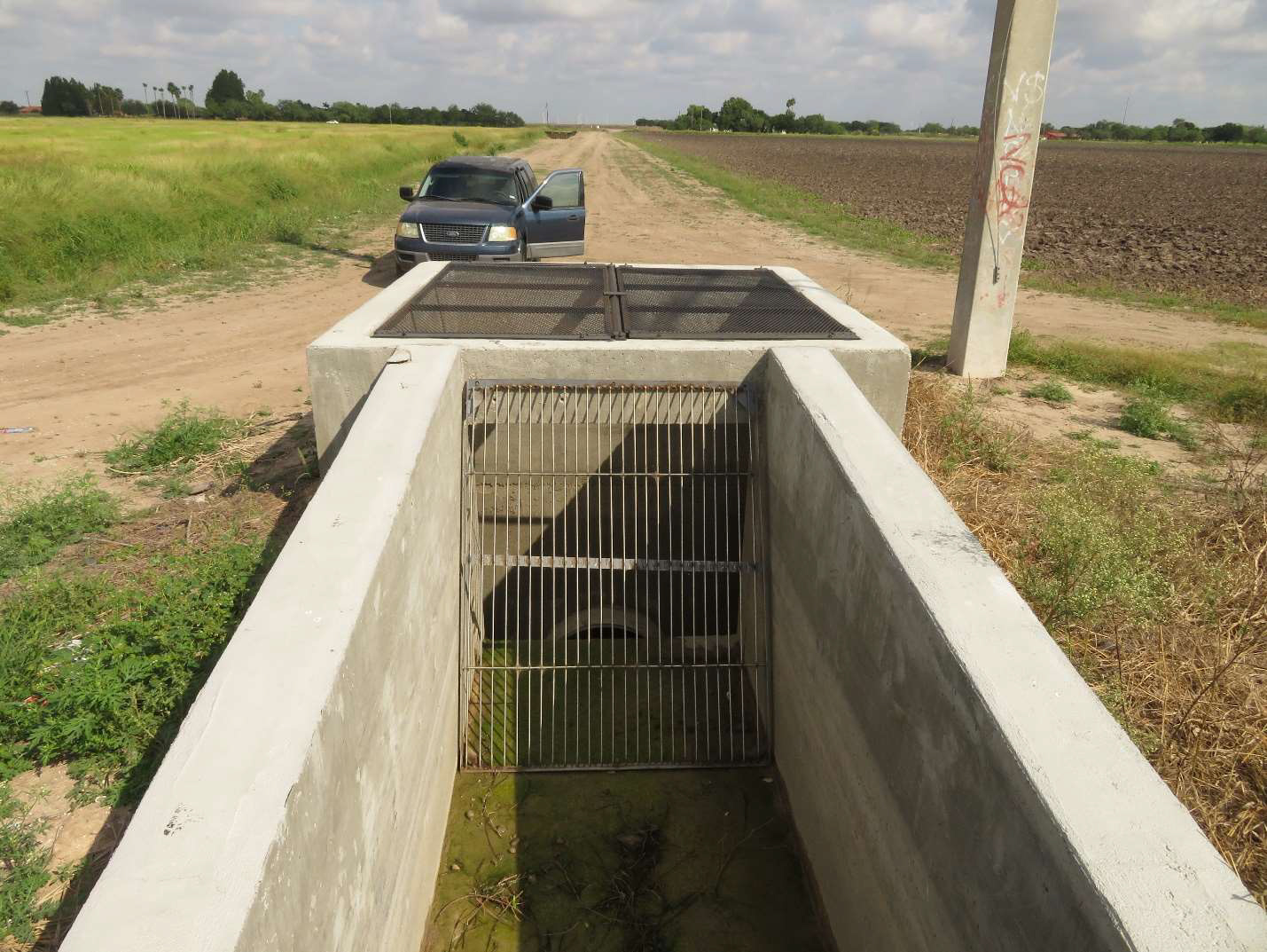 A canal structure and pipe with a grating on it. It is located in agricultural field.