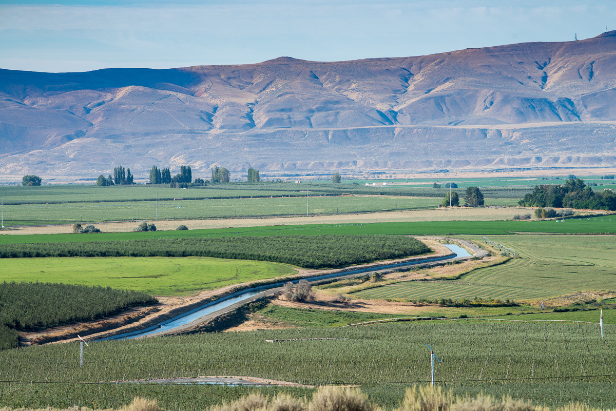 A canal flowing through a valley with agricultural fields around it.
