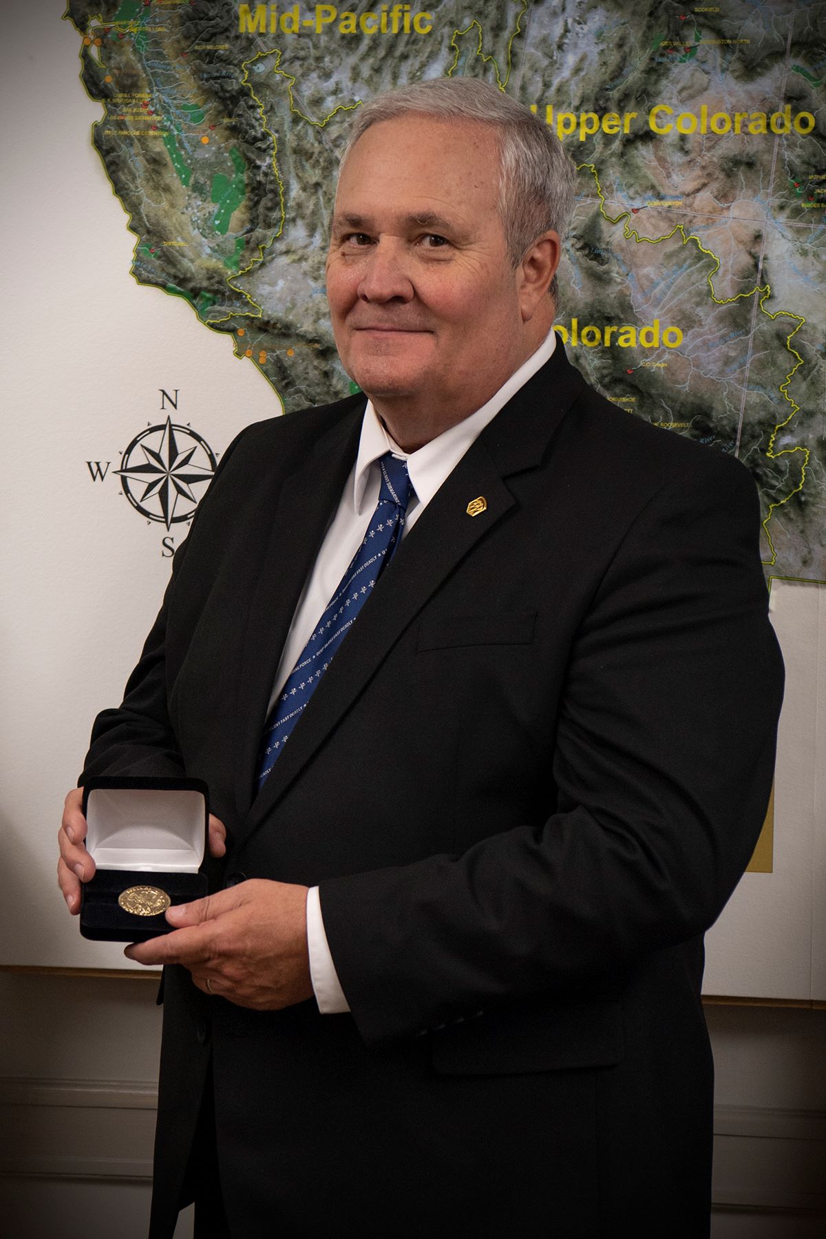 A person posing holding a medal with a map of the Western United States behind them.