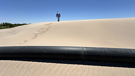 A man walks up a large pile of sand.