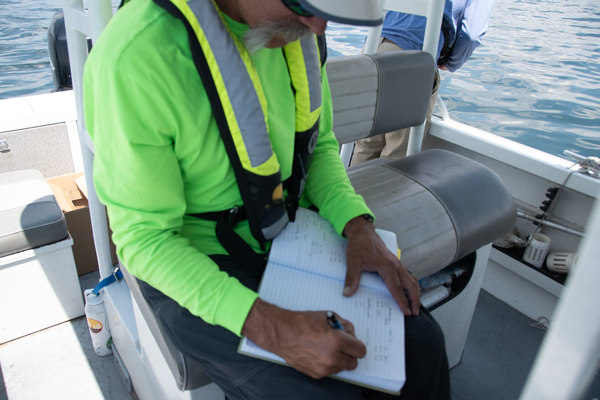 Reclamation scientist writing in a logbook on his lap at the helm of the boat.