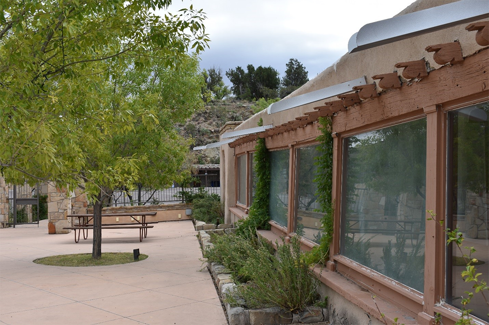 a one story building sits atop a stone retention wall surrounded by trees and walkways