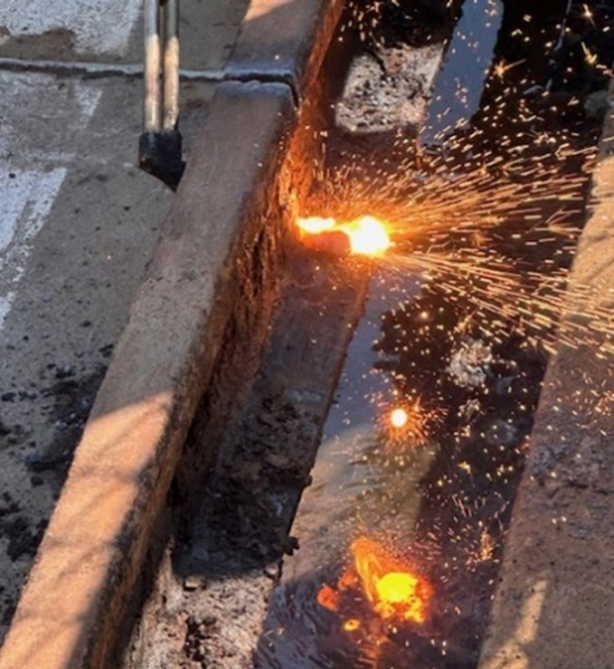 The rusted bolts of the original rail system are cut by torch for removal.