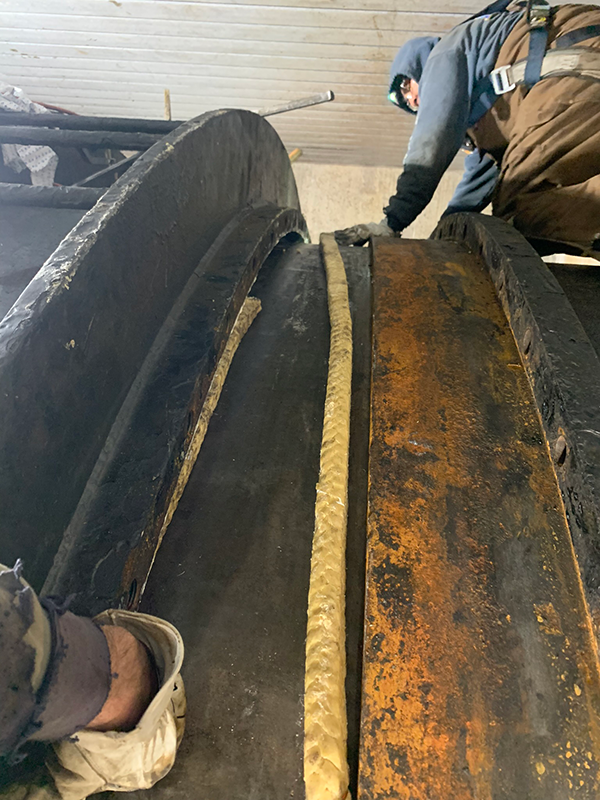 Plant mechanic Randy Sloan kneels on top of a penstock as he and a coworker tuck new packing material into the small space under the flange. Crews placed six layers of new packing material in the space to create a water-tight seal to guard against future leaks. 