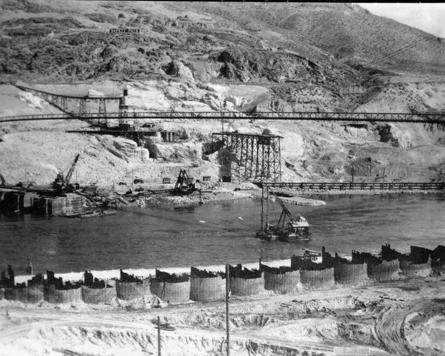 Photo taken August 8, 1936. Cross river spoils conveyor going to Rattlesnake Canyon center with west mix plant behind. Low Wakefield cofferdam on eastside in foreground at Grand Coulee Dam.