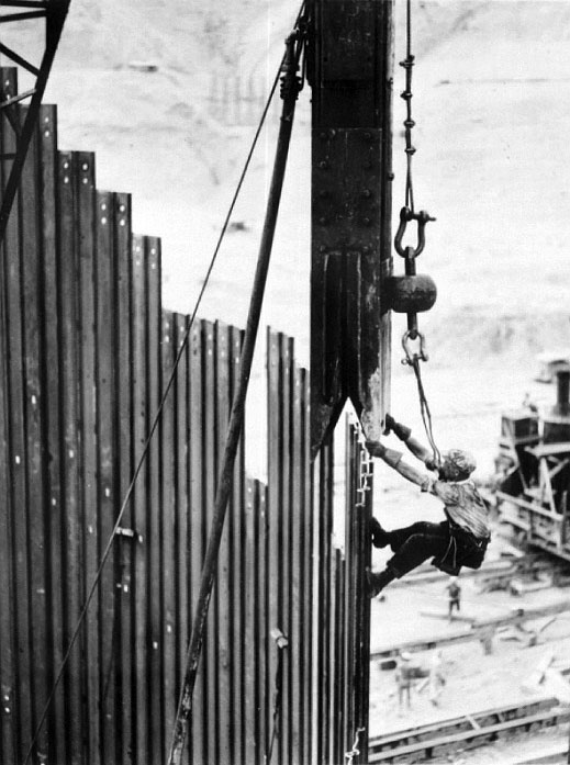 Photo taken August 1936. Setting a 3 1/2 foot ton steam hammer for driving piles in cofferdam connecting section “C” with block 40.