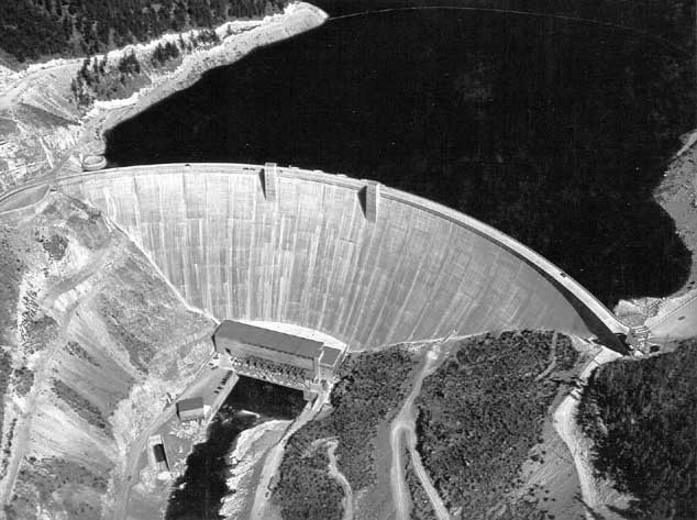 Aerial oblique view of Hungry Horse Dam and powerplant. Just above left crest of dam is glory hole spillway. Discharge portal is seen below river outlet valve house at lower left. Elevation level of reservoir is 3529.77 and storage is 2,796,659 acre-feet. August 7, 1953.