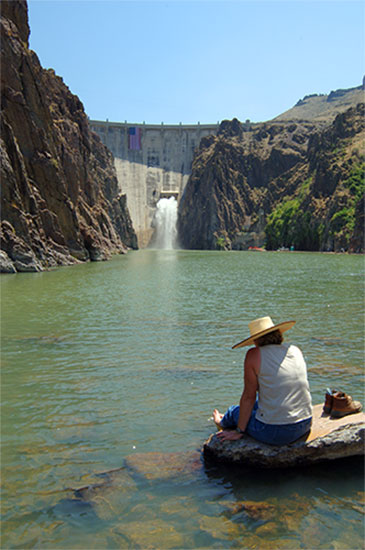 Lady sitting in water looking at Owyhee Dam in Oregon.