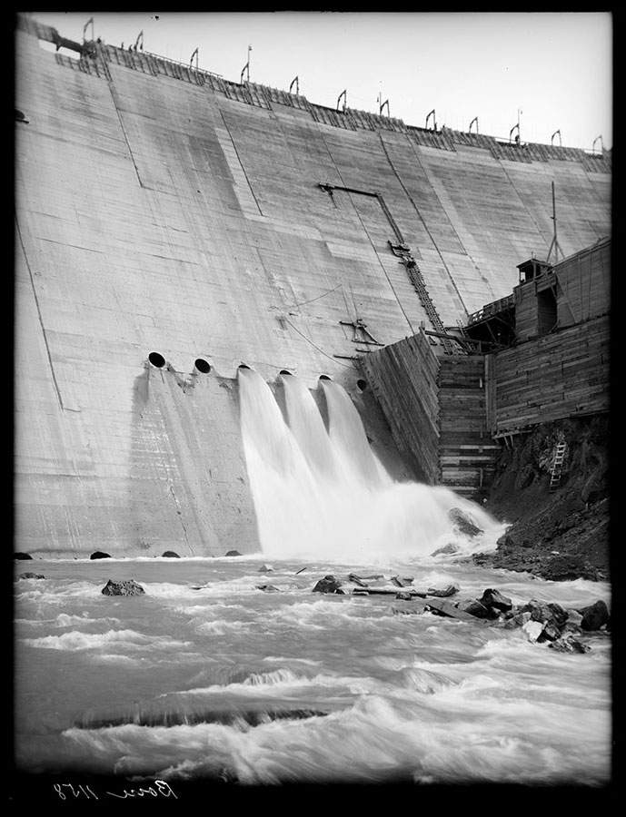 Arrowrock dam site. Portion of downstream face of dam showing water coming through middle outlets. Note bulkheads to protect concrete plant from spray. The first outlets are operating under 51 ft. head.