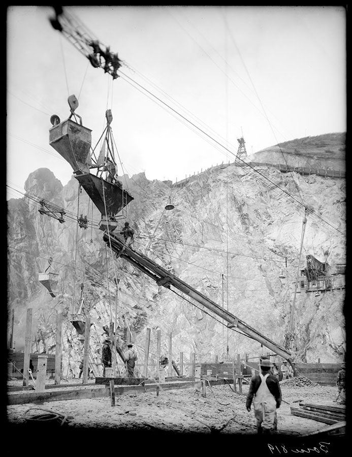 Arrowrock dam site. Concrete distributing system. Conveying bucket dumping concrete into cableway hopper and through chute into palce in the dam.