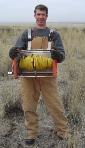(Left) February 2004 Geophysicist with portable cable spool and cable equipment used for electrical resistivity testing. The resistivity tests are conducted over broad areas and provide data on the density and permeability of subsurface materials.