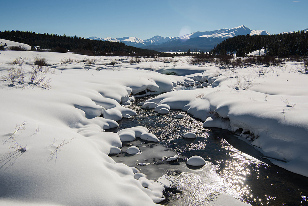 A photograph of snow and a running stream in a mountain meadow.