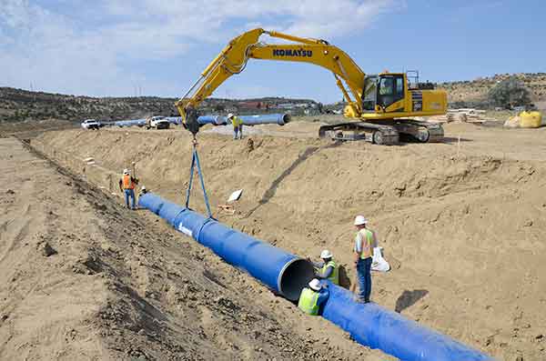 Construction crew using an excavator to place a section of pipe along Reach 12A of the Navajo-Gallup Water Supply Project