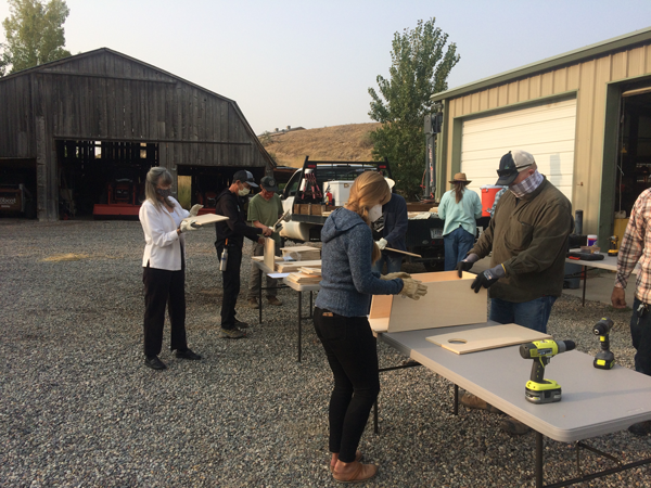 Eight volunteers assemble wood pieces for bird boxes on tables outside of a warehouse at the Grand Junction Wildlife Area. Photo by Justyn Liff