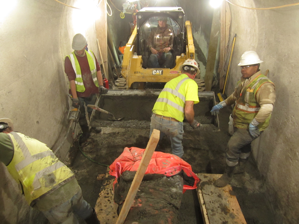 A yellow skid steer delivers concrete in the Paonia Dam tunnel invert while four contractors in safety gear place the concrete. Photo by Matt Bryner 