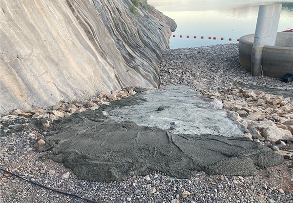 A steep gray gravel access road down to the morning glory spillway in Ridgway Reservoir. Reservoir water and orange buoys are visible in the background.