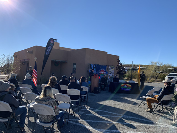 Outdoor view of nine professionals in hardhats turning dirt with shovels.  Several pieces of heavy equipment are parked in the background. 